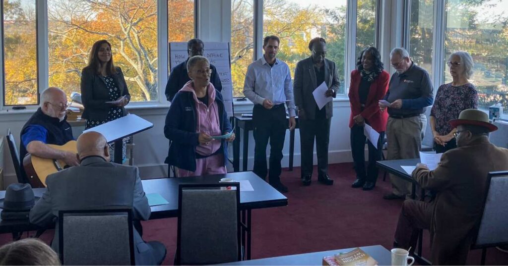 Chaplains singing together accompanied by a guitar in a room with large windows.